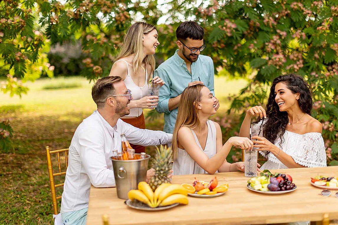 Group of young people cheering with fresh lemonade and eating fruits in the garden

 
